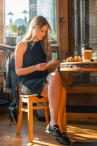 A woman seated at a cafe table wearing the Everyday Merino Dress in black, with a book and coffee in front of her