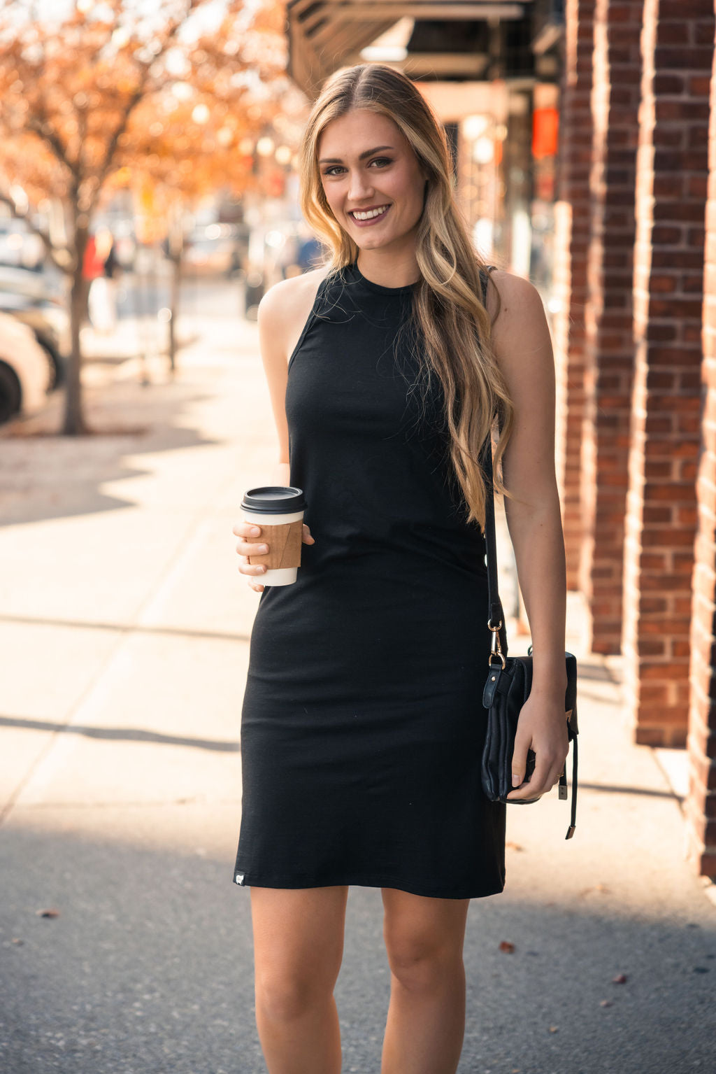 A woman wearing the Everyday Merino Dress in black paired with heels and holding a coffee mug